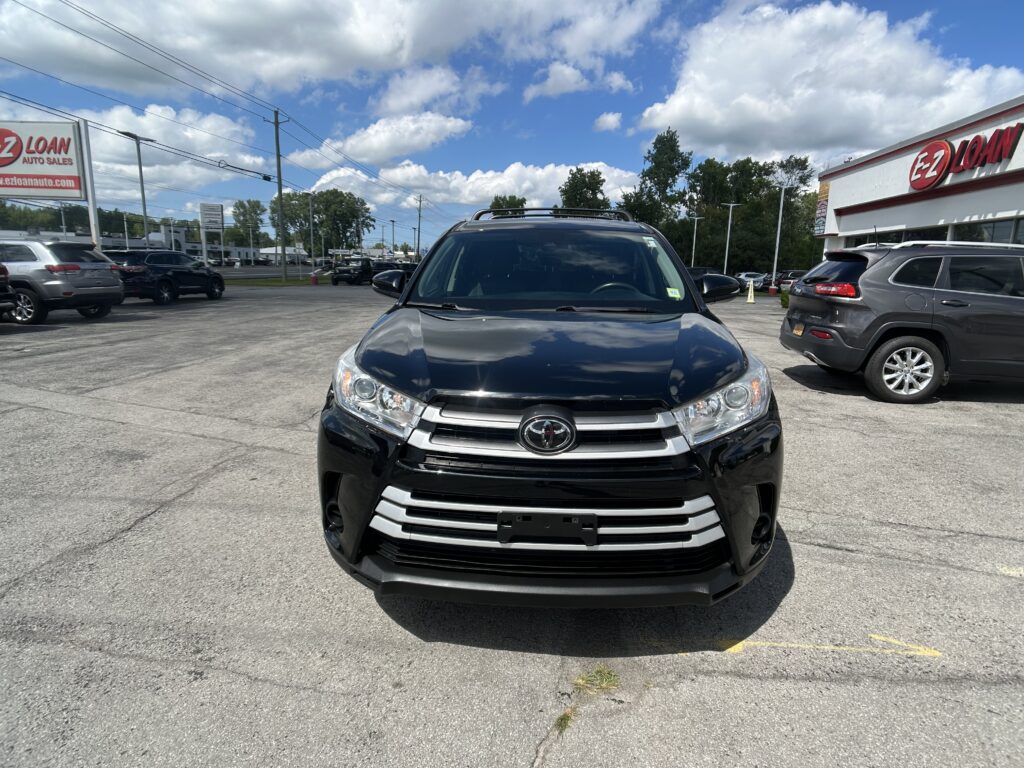 Front view of a black SUV parked in a dealership lot, with an E-Z LOAN building on the right and other cars around.