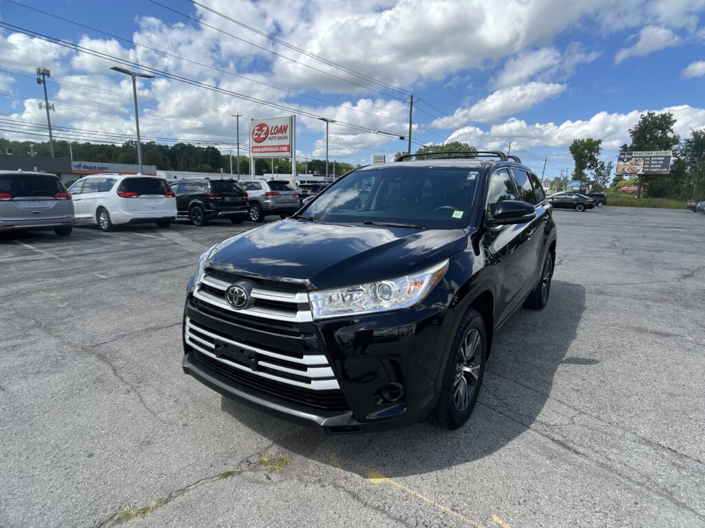 Close-up of a black Toyota SUV in a car dealership lot with other cars and an EZ Loan Auto Sales sign in the background on a sunny day.