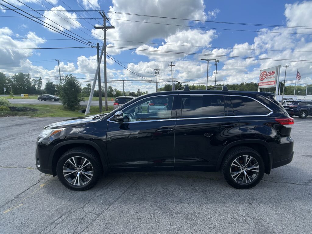 Black SUV in a parking lot under a blue sky with power lines and a billowing cloud-filled backdrop, car roof racks visible at the top edge