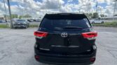 Rear view of a black Toyota Highlander SUV parked in a lot with other cars and a cloudy blue sky above.