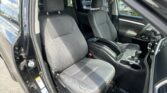 Interior of a dark SUV with two front seats in gray fabric, center console visible, and the driver’s door open.