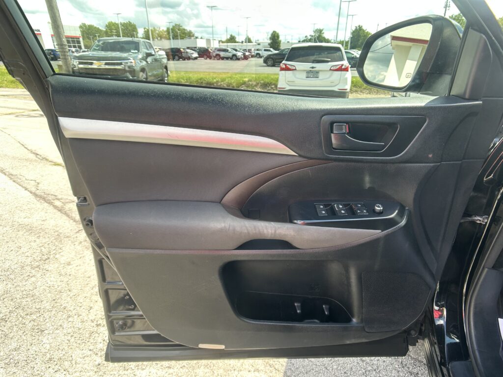 Interior of a car door panel with window controls and door handle, next to a side mirror and outside parking lot scenery in view.