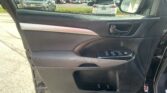 Interior of a car door panel with window controls and door handle, next to a side mirror and outside parking lot scenery in view.