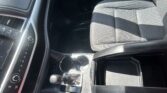 Interior of a car showing the center console with climate controls, gear shifter, and cup holders, next to a gray patterned front passenger seat.