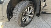 Close-up of an SUV tire on an alloy wheel, with the wheel well and a rusty suspension component visible behind it.