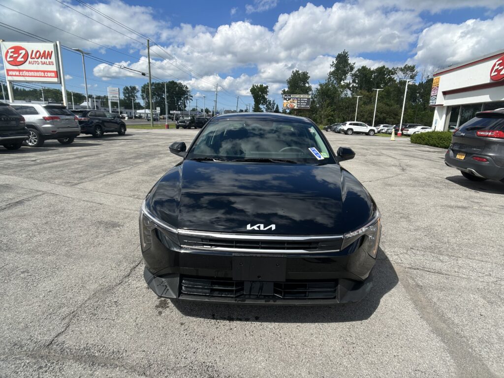 Front view of a black Kia SUV in the dealership lot, with other parked cars and an E-Z Loan Auto Sales sign in the background on a sunny day.