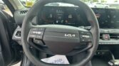 Steering wheel of a Kia with a full digital instrument cluster and a wide horizontal touchscreen displaying vehicle info.