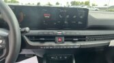 Wide view of a car interior showing a large center touchscreen with radio app icons and time beside a parking lot outside the windshield.