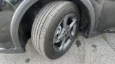 Close-up of a car's front left wheel and tire in the fender well, with water droplets on the body and wet pavement nearby.