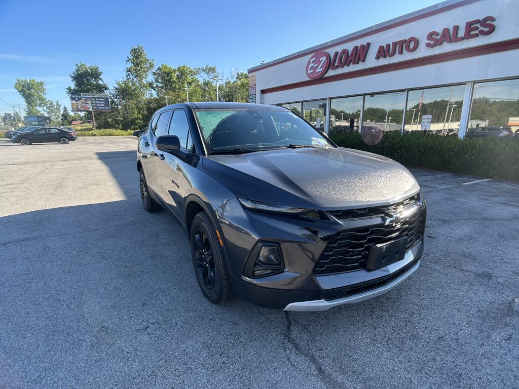 Gray SUV in a parking lot in front of an E-Z Loan Auto Sales storefront on a sunny day.