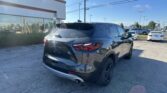 Dark gray SUV parked in a dealership lot beside a glass-front building on a sunny day with a blue sky.