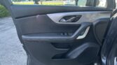 Interior of a car door with black and gray trim, window controls, and an open door; parking lot with cars outside in the background.