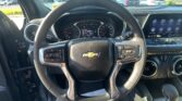 View from driver seat showing steering wheel, instrument cluster, and a touchscreen infotainment display in a Chevrolet interior; outside parking lot visible through windshield.