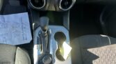Center console of a car showing two round air vents, a touchscreen infotainment display above, and a gear shifter with cup holders nearby.