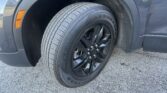 Close-up of a car wheel and tire with black alloy rim, visible tread pattern, and an orange side marker on the fender nearby.