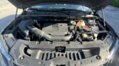 Open car hood revealing engine bay with air intake hose, battery, and coolant reservoir visible under sunny sky