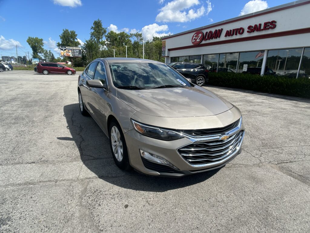 Silver Chevrolet sedan parked diagonally in front of EZ Loan Auto Sales storefront under a blue sky.