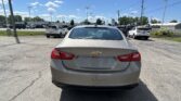 Rear view of a beige Chevrolet Malibu LT parked in a dealership lot with other cars under a clear blue sky.