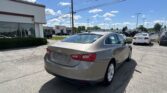 Rear view of a silver Chevrolet sedan in a car dealership lot with a Toyota showroom in the background, under a blue sky.
