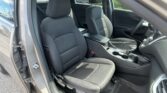 Front interior of a car with black fabric seats, center console, and steering wheel visible through an open driver’s door.