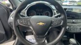 View from the driver’s seat of a Chevrolet with the steering wheel, instrument cluster, and center touchscreen visible; a parking lot with cars is outside the windshield.