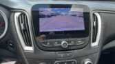 In-dash backup camera view of a parking lot with orange guiding lines on the screen behind the car.