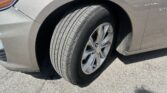 Close-up of a Chevrolet SUV's front left wheel, tire and silver alloy rim, with the gray body and headlight partially in view.