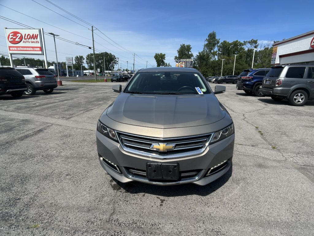 Front view of a silver Chevrolet SUV parked in a car lot with other vehicles and an E-Z Loan sign in the background on a sunny day.