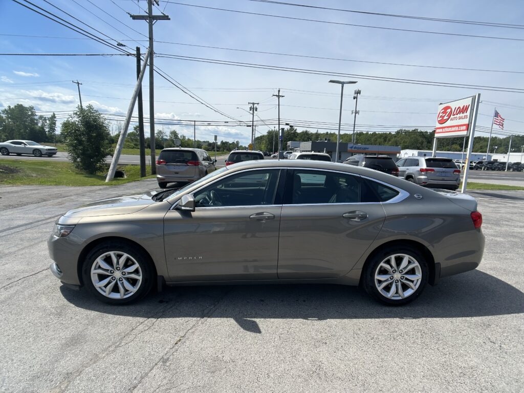 Front side of a gray Chevrolet Impala in a car dealership lot, with a large EZ Loan Auto Sales sign in the background.