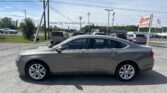 Front side of a gray Chevrolet Impala in a car dealership lot, with a large EZ Loan Auto Sales sign in the background.