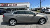 Silver Chevrolet Impala sedan in the foreground at a car dealership lot, with the E-Z Loan Auto Sales building on the left and a Toyota dealership in the distance under a blue sky.