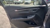 Open car door interior with stitched black panel; parking lot with white and gray SUVs outside.