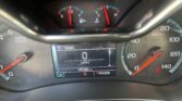 Close-up of a car instrument cluster showing a digital speed readout at 0 MPH, odometer at 100,384 miles, and gear indicator (PRNDM) with a tachometer and fuel/temperature gauges surrounding it.