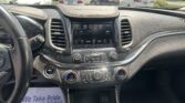 Studio-style view from the car cockpit showing the center touchscreen, climate controls, and gear shifter with a parking lot of white cars outside the windshield.