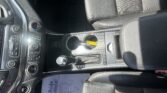 Interior of a car showing center console with gear shifter, two cup holders, and a yellow tag in the holder, black leather seats far right and left
