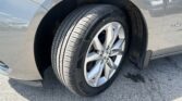 Close-up of a silver car's front wheel with a dark tire and alloy rim, showing dirt around the wheel well and fender area.