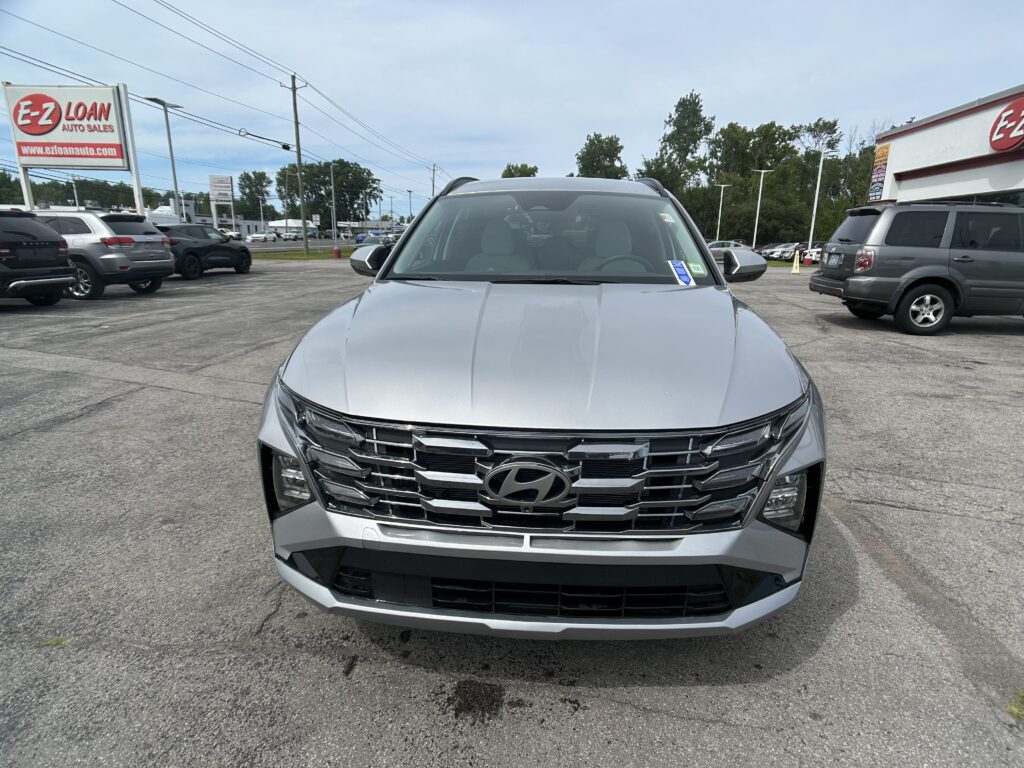 Front view of a silver SUV at a car dealership, showing the prominent Chevrolet grille and badge with other vehicles and an E-Z Loan sign in the background.