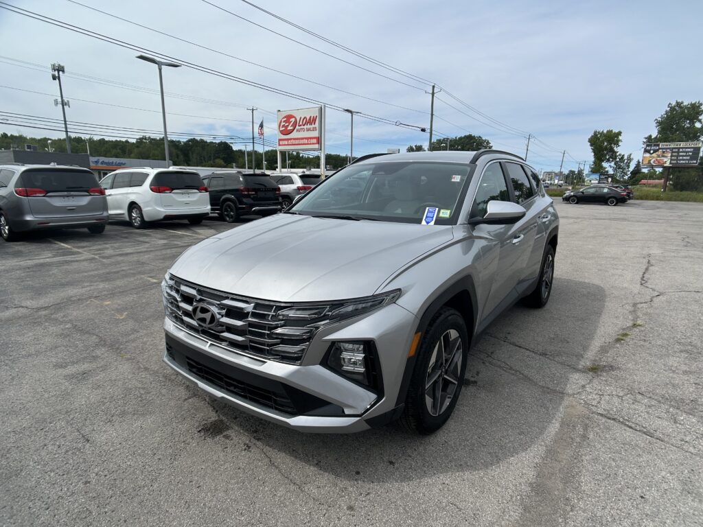 Front corner of a silver SUV in a car dealership lot with other vehicles and an EZ LOAN sign in the background.