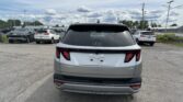 Rear view of a silver Hyundai Tucson in a car dealership parking lot with other vehicles and cloudy sky above