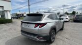Rear view of a silver Hyundai SUV parked in a car dealership lot with other vehicles and a white building in the background.