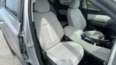 Inside view of a gray car’s front seats and center console, door open to a parking lot outside.