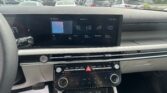Car dashboard touchscreen showing apps like FM, Phone, and Vehicle Diagnostics; parking lot visible through windshield, daytime.