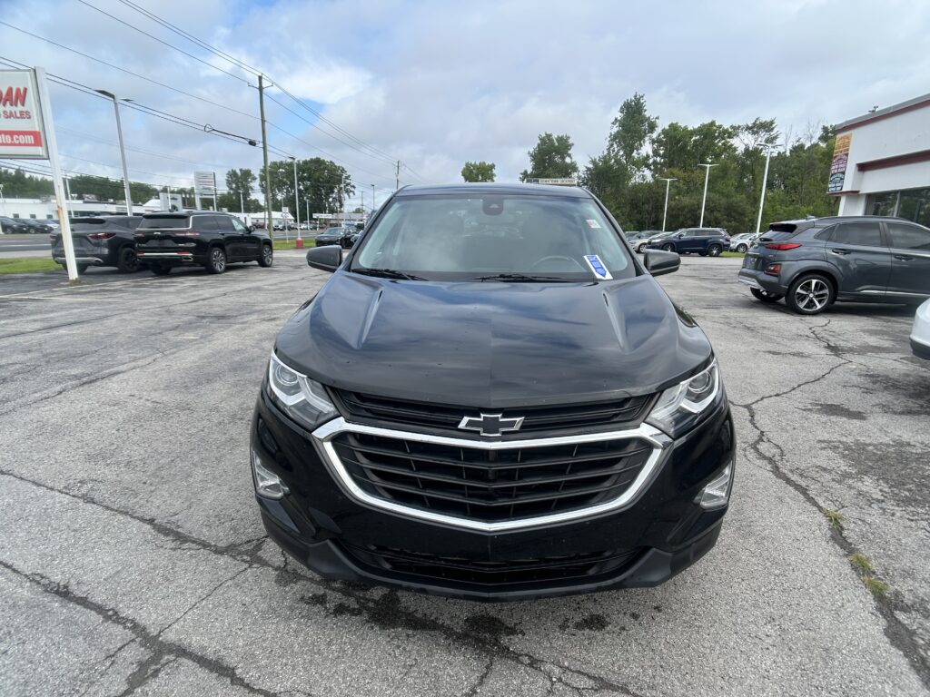 Front view of a black Chevrolet SUV in a dealership parking lot, with other vehicles and a building in the background for context.