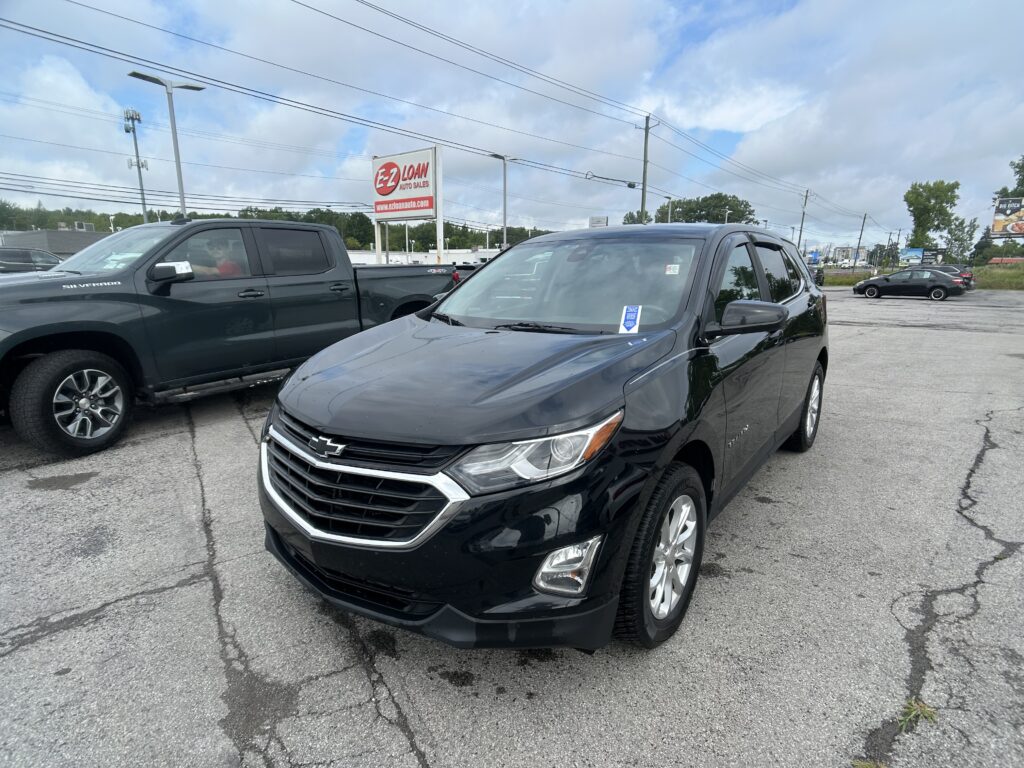 Front-right view of a black Chevrolet SUV in a dealership parking lot, with an EZ Loan Auto Sales sign and cloudy sky in the background.