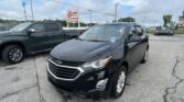 Front-right view of a black Chevrolet SUV in a dealership parking lot, with an EZ Loan Auto Sales sign and cloudy sky in the background.