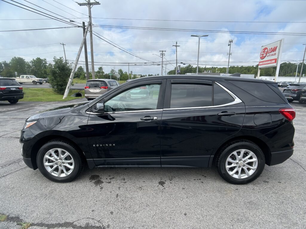 Close-up of a black Chevrolet Equinox parked in a lot with an E-Z Loan Auto Sales sign in the background and cloudy sky above.