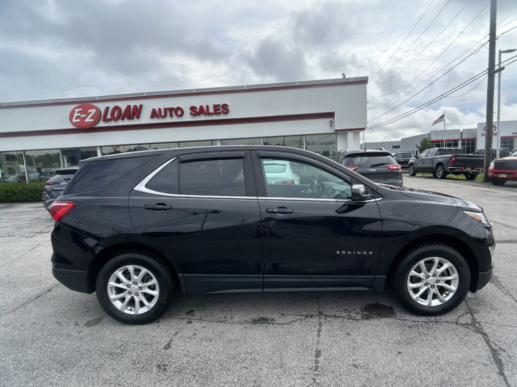Black Chevrolet Equinox in the foreground at an E-Z Loan Auto Sales lot with other cars and a dealership building in the background