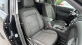 Interior of a car showing two front seats with textured black upholstery and orange stitching, center armrest and partial dashboard.