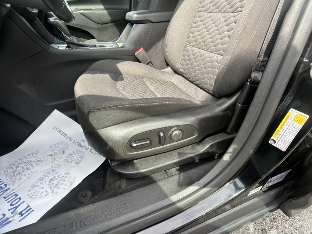 Front car interior showing driver seat and center console with a red seatbelt buckle visible, papers on the floor mat nearby