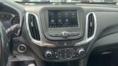 Center console touchscreen in a car displaying apps (Audio, Phone, Wi‑Fi, Settings) with Apple CarPlay and Android Auto while parked in a lot.